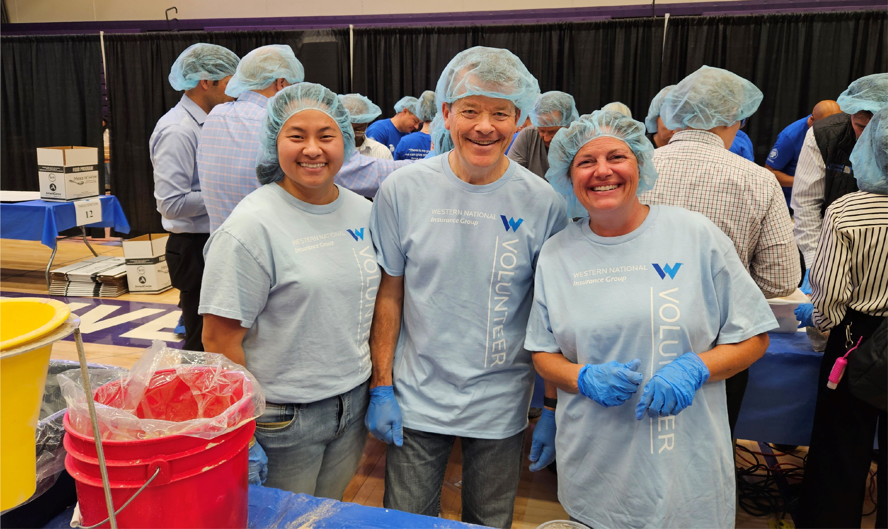 Western National employees smiling for the camera in their volunteer t-shirts and hair nets packing meals.
