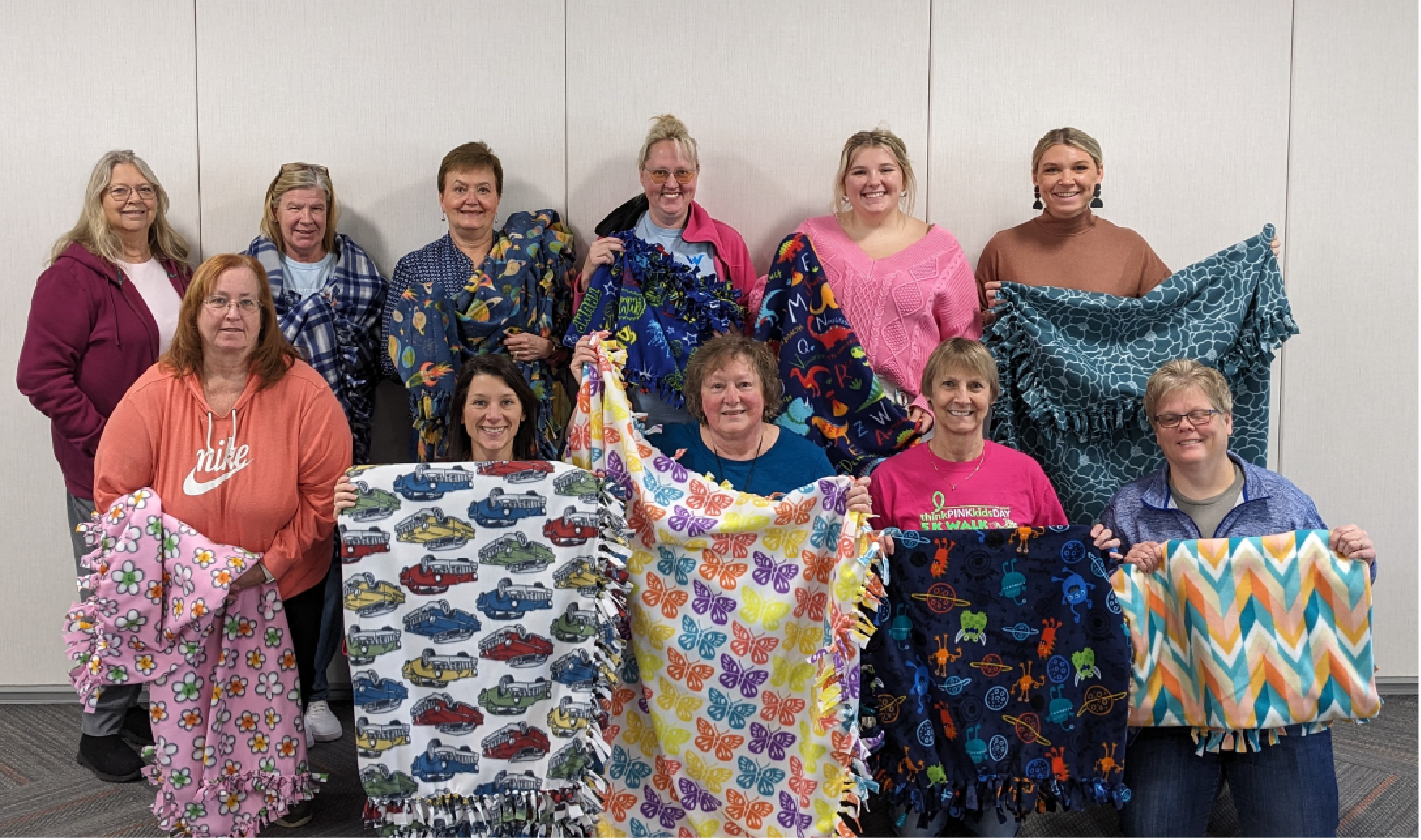 Western National employees smiling for the camera and holding up blankets that they helped make for Project Linus.