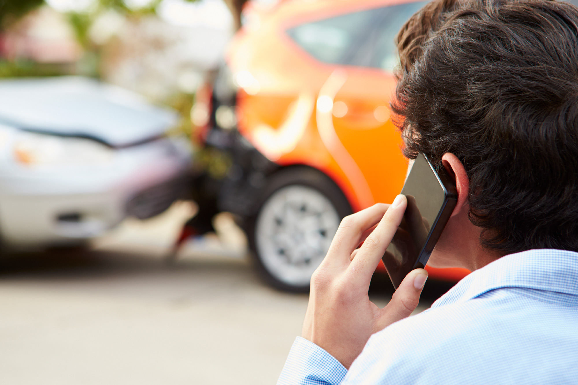 Back of young man's head, holding a cellphone at the scene of an accident.