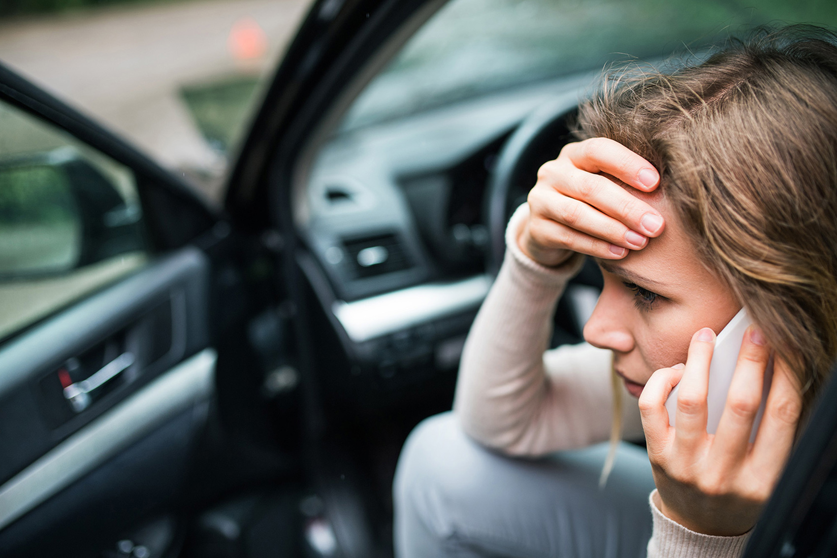 Woman sitting in her vehicle, looking distressed, and talking on phone after being involved in a car accident.