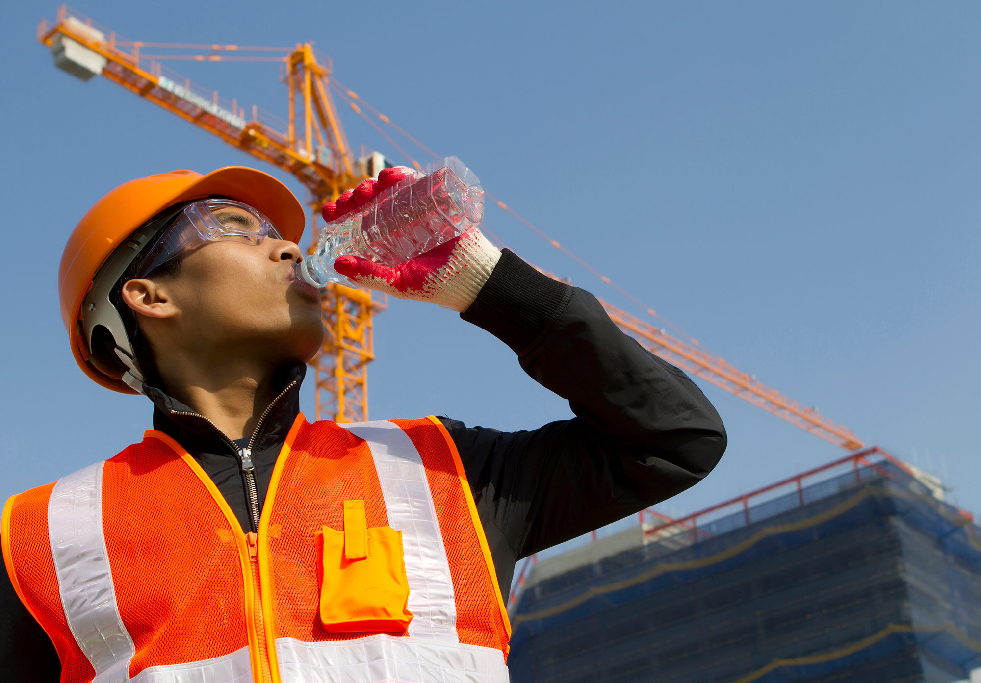 Construction worker in protective hear drinking from a water bottle.