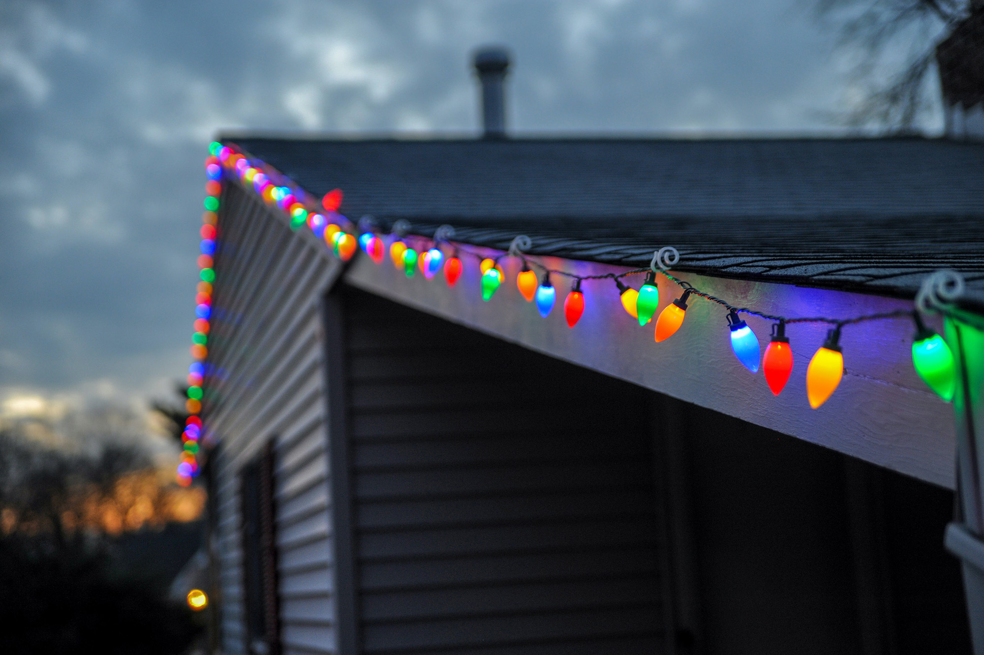String of colorful lights hung along the edge of a roof on a house.