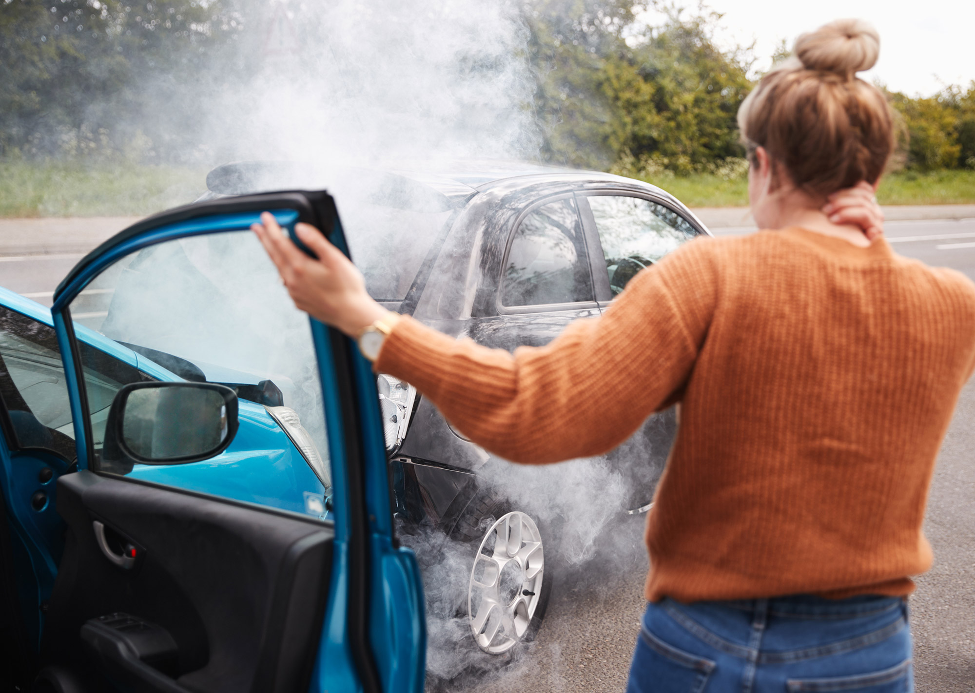 Woman stepping out of car after colliding with another vehicle, which can be seen in the background.