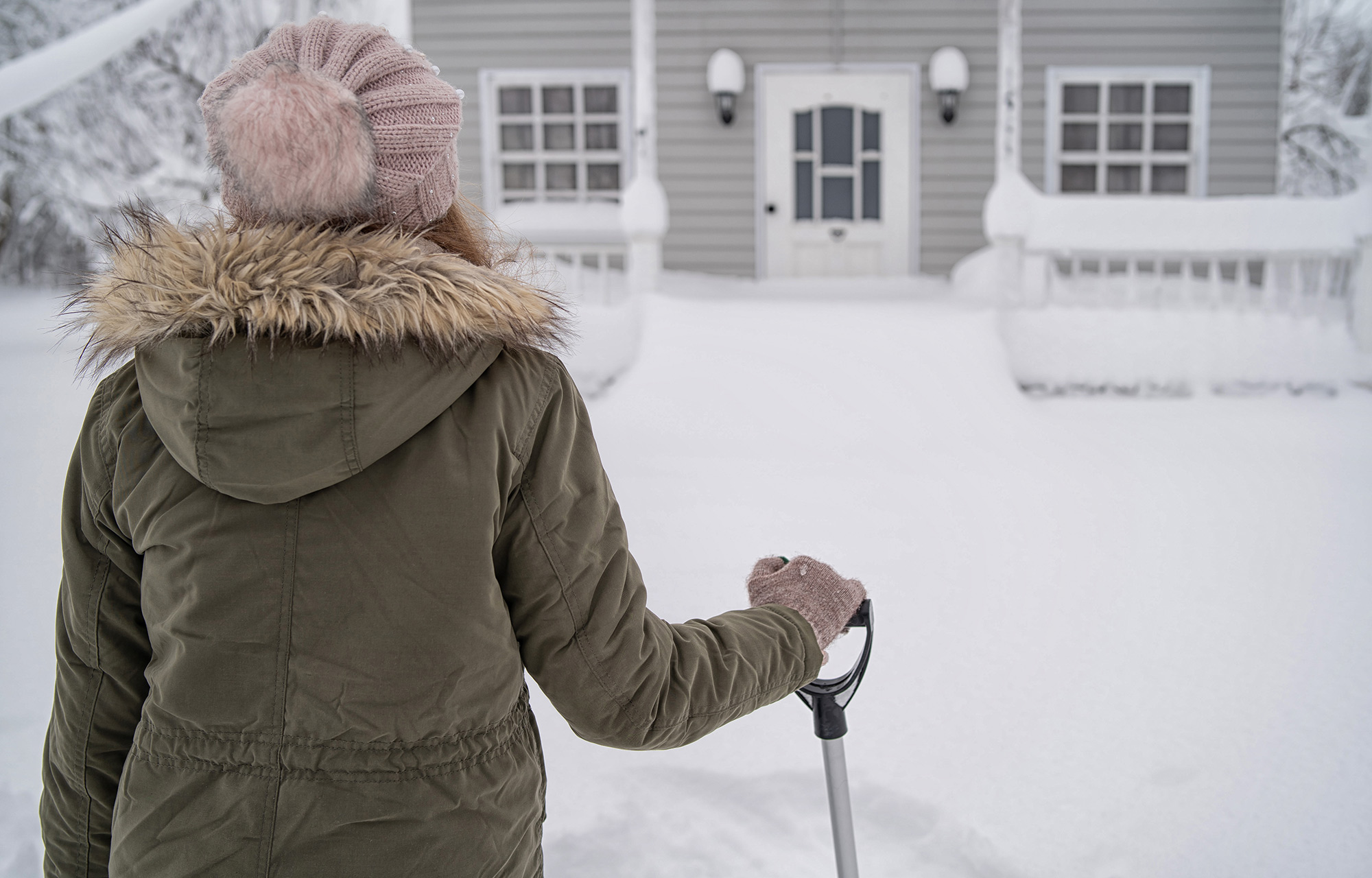 Woman in winter hat and coat looking out over snowny scene in front of house.