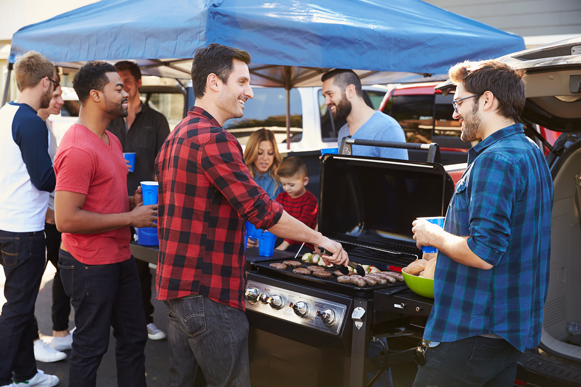 A group of young men in flannel shirts near a tent, grilling