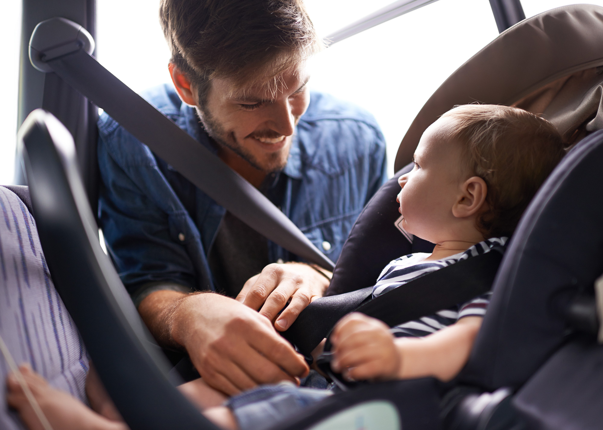 Father buckling his baby into a carseat in the back of a vehicle.