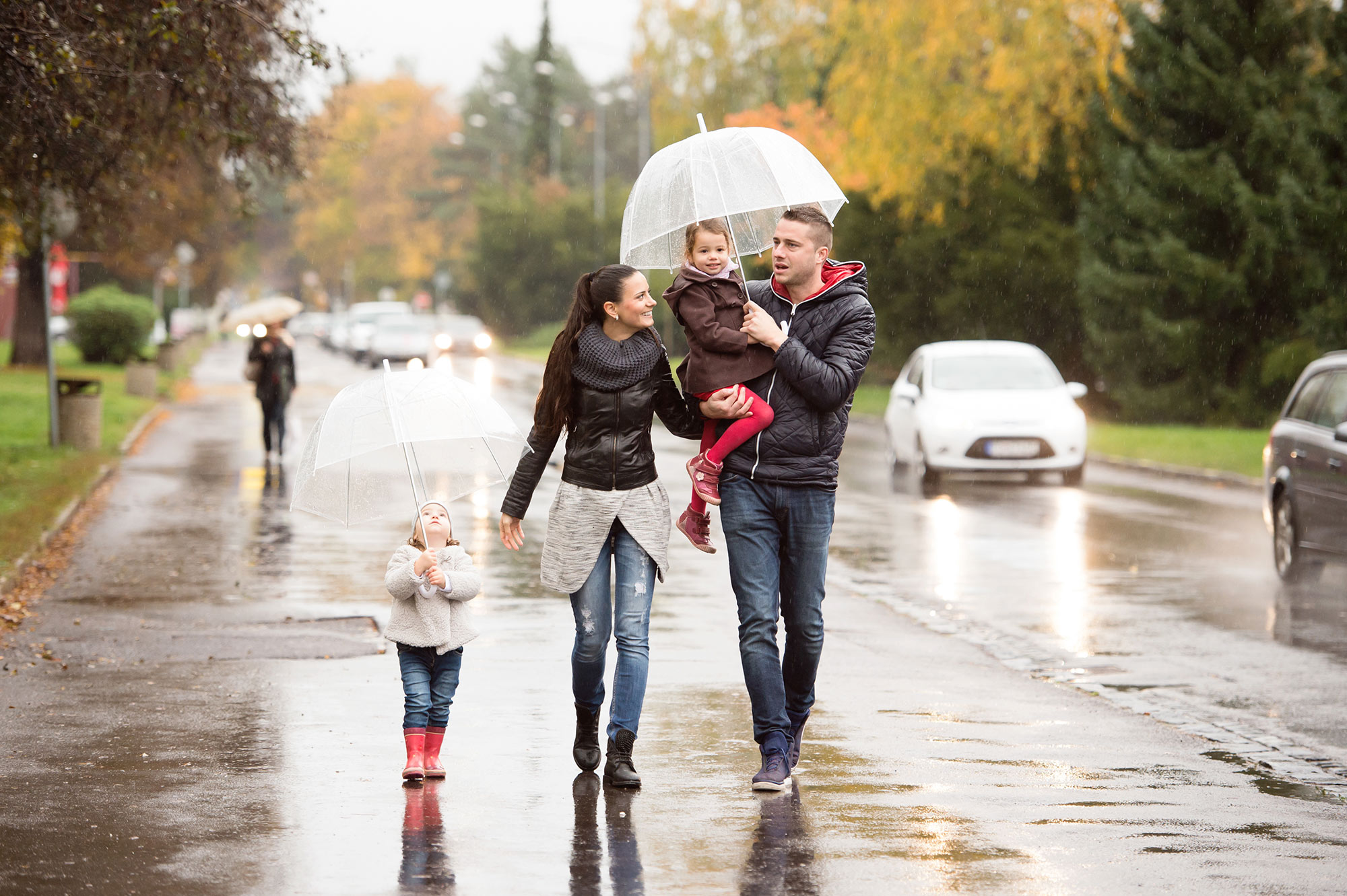Family of three walking in the rain with a clear umbrella.