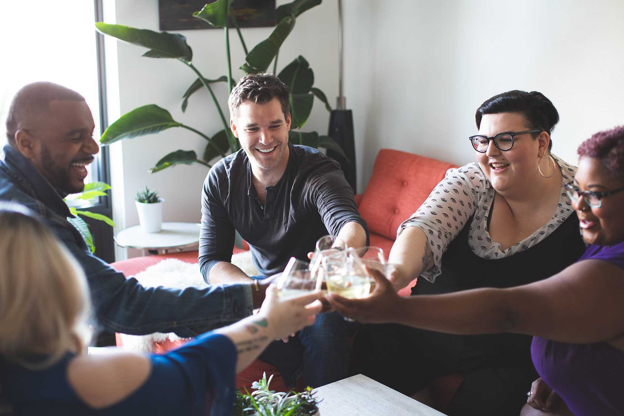 Diverse group of friends sitting in a living room, clinking glasses together in a toast.