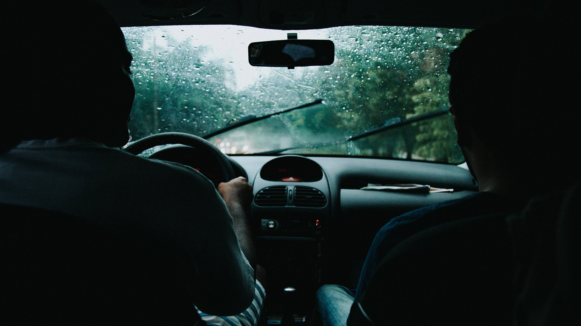 View of rain on vehicle windshield and windshiled wipers from the back seat of the vehicle.