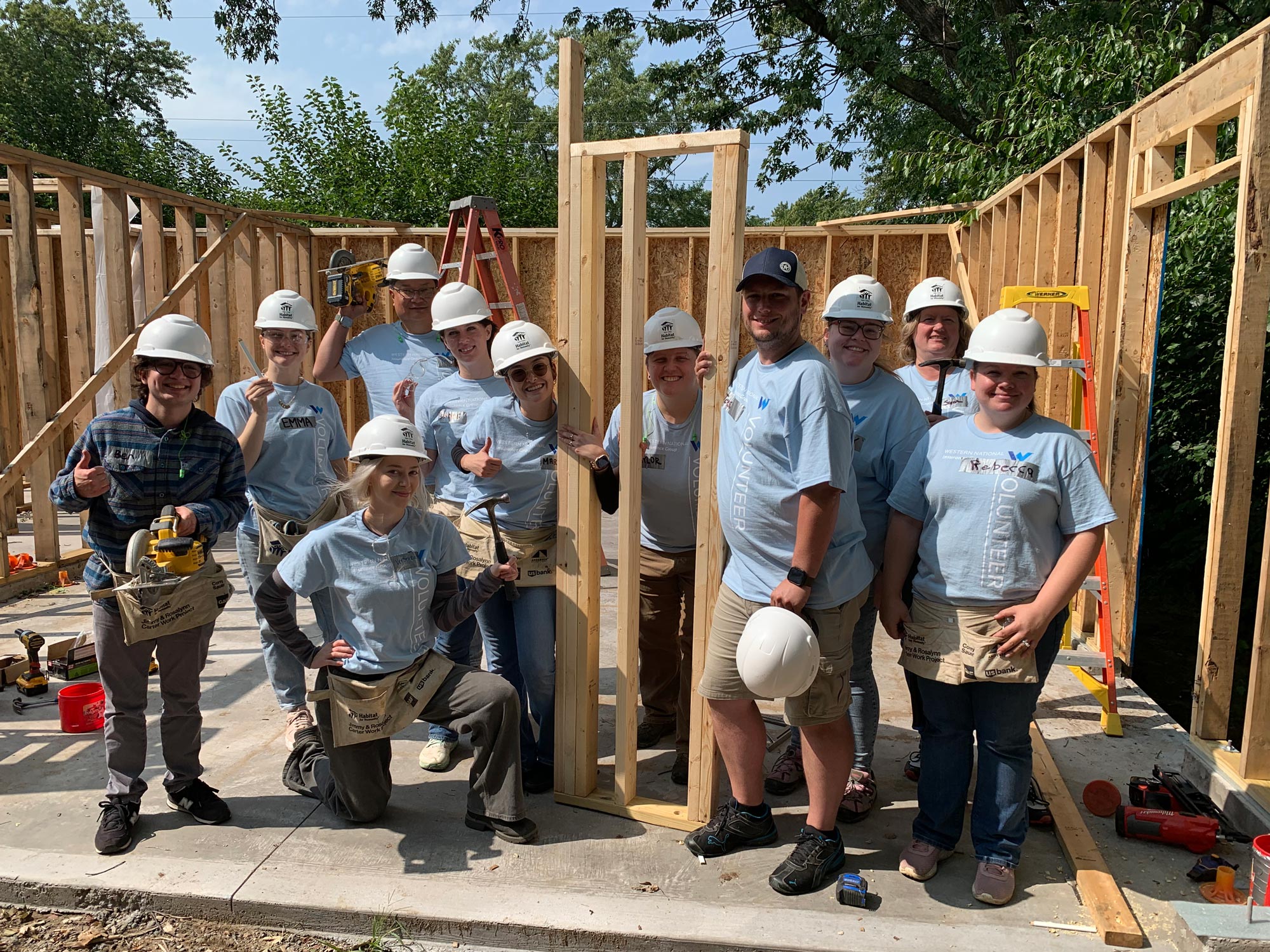 A group of employees, in volunteer shirts and hard hats, smiling for the camera at a volunteer build site.