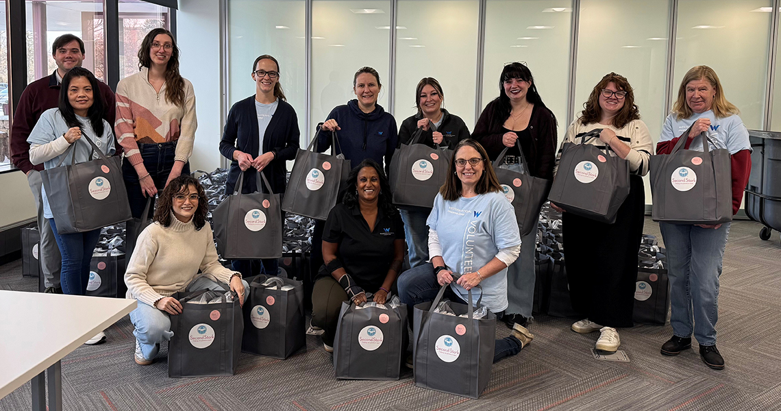 Western National employee volunteers wearing matching Western National branded t-shirts and posing for a group photo in a warehouse with wooden dressers they built during a volunteer event.
