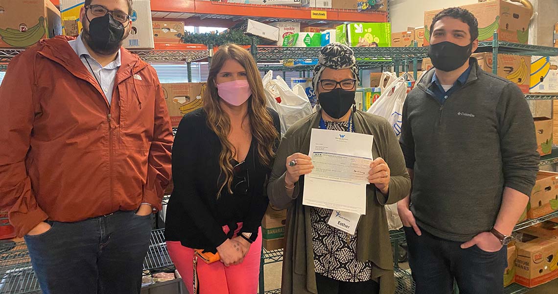 Four Western National employee volunteers wearing facemasks posing for a photo in front of shelves of food items at a food bank.