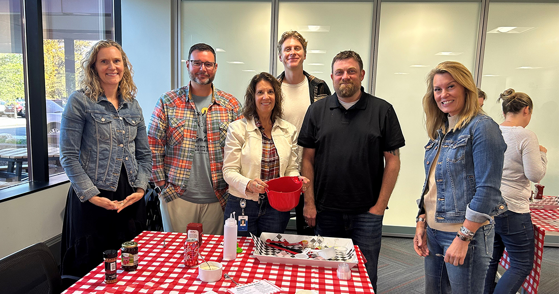 Six Western National employees wearing sunglasses posing together outdoors on a sunny spring day with the exterior of Western National's Edina office building in the background.